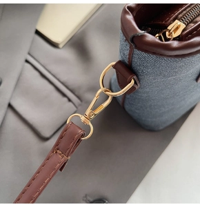 Detail of blue denim bucket bag featuring brown leather trim and gold metal hardware