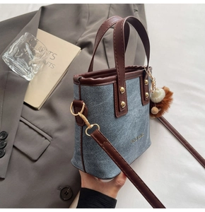 Detail of denim and leather bucket bag with furry charm on a clean background