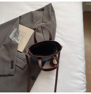 Flat lay of blue denim bucket bag with brown leather trim and plush ball charm detail