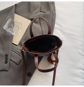 Close-up of stylish brown leather and blue denim bucket bag with plush charm and zip pocket