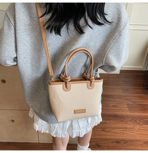 Close-up of beige woven bucket bag with leather handles and metallic fashion plaque