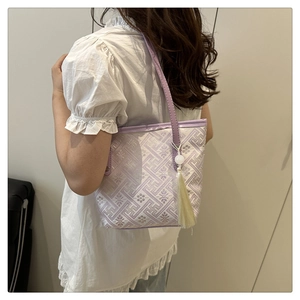 Detail of light purple tote bag with geometric jacquard and cream tassel charm accessory