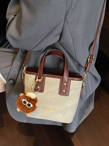 Retro canvas bucket bag with brown leather straps and plush charm on a grey suit jacket