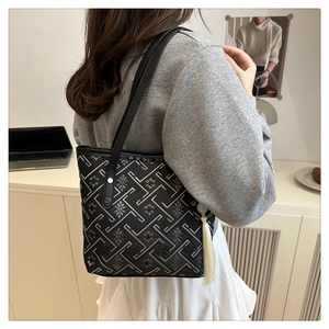 Detail of a black tote bag featuring silver maze embroidery and a white tassel pendant