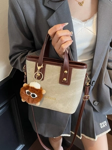 Vintage canvas bucket bag with brown faux leather trim and plush charm worn with a grey blazer