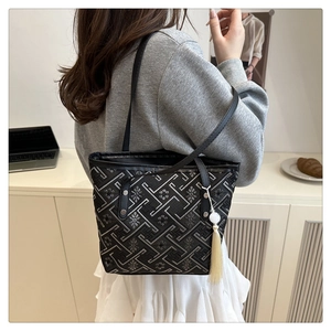 Dettaglio borsa tote nera con motivi geometrici, manici in pelle e ciondolo con nappa