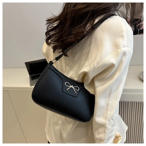 Close-up of black shoulder bag featuring litchi texture and a gold metal bow buckle