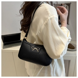 Detailed view of black underarm bag with litchi texture and golden bow ornament