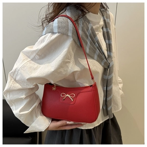 Detail of red textured leather underarm bag with gold bow and flower zipper on model