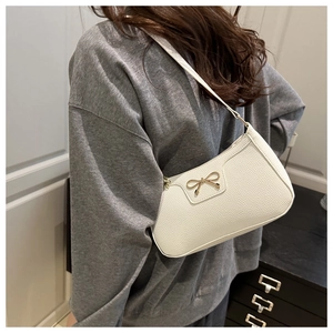 Close-up of white lychee leather underarm bag with gold bow ornament worn by a model