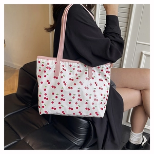 Close-up of a white tote bag featuring cherry patterns and pink faux leather straps