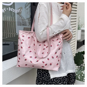 Detail of pink strawberry print tote bag with long handles shown in street setting
