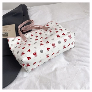 Détail du sac cabas imprimé ours et cœurs avec livre et blazer posés sur un lit blanc