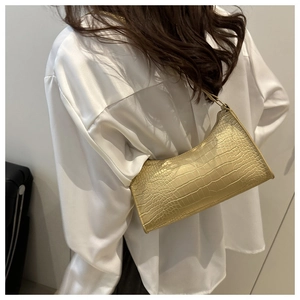 Detail of gold crocodile texture on baguette bag with glossy finish and zipper