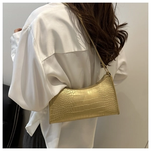 Detail of metallic gold crocodile pattern handbag worn on shoulder with satin blouse