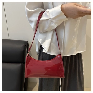 Detail of burgundy patent leather shoulder bag held by a model in a white shirt