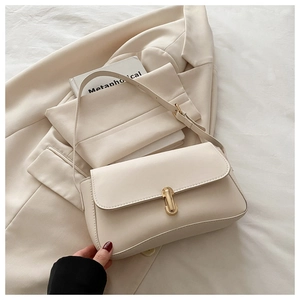 Detail shot of a cream leather crossbody bag with a rectangular gold buckle on a blazer
