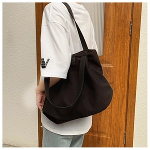 Vue latérale d'un grand sac cabas en toile noire avec large bandoulière par un mannequin