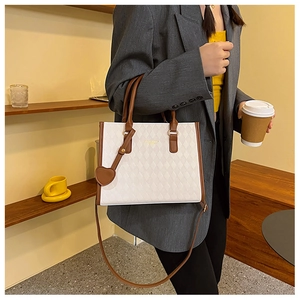 Close-up of a white quilted tote bag with brown handles and a heart charm on a grey blazer