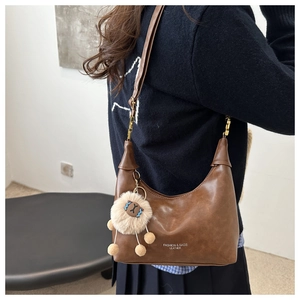 Close-up of brown matte leather dumpling bag with plush charm and golden hardware detail