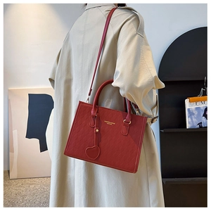 Red woven tote bag with heart charm shown on beige trench coat model in modern interior