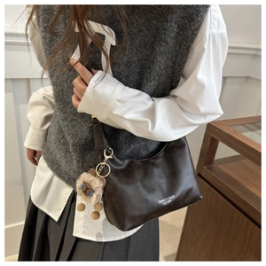 Detail of dark brown leather crescent bag featuring fashion logo and plush charm