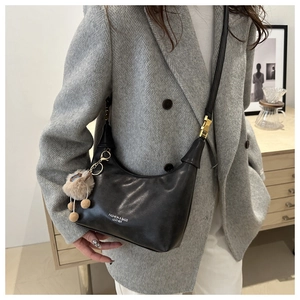 Detail of black leather hobo bag with white typography and a plush fur ball charm