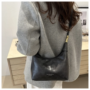 Detail of black glossy leather hobo bag with gold hardware and white text print