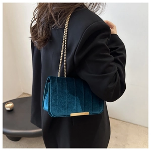 Detail of dark green velvet crossbody bag with gold chain and vertical quilted pattern