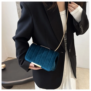 Detail of teal velvet crossbody bag with vertical quilting and gold chain strap