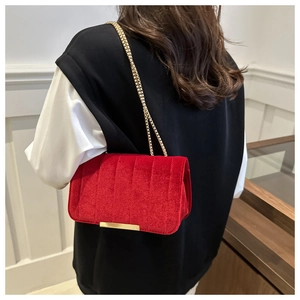 Detail of red velvet crossbody bag with vertical quilting and gold chain strap