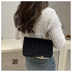 Detail of a black velvet square chain bag styled with a white tweed top and jeans