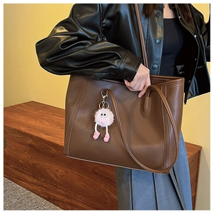 Detail of dark brown tote bag with pink plush monster charm on an autumn outfit