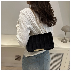 Close-up of black velvet crossbody bag with gold chain strap on knit sweater