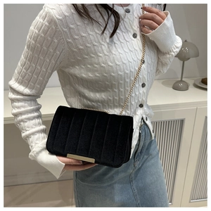 Detail of black velvet crossbody bag with gold chain and vertical striped texture on a model