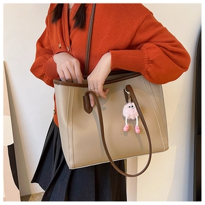 Large beige tote bag with brown leather trim and a cute pink plush charm on model