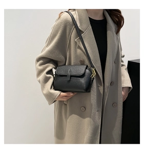 Detail of black lychee grain leather crossbody bag with gold buckle on beige coat