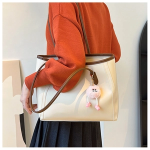 Cream tote bag with brown trim and plush charm shown on a model in a stylish interior
