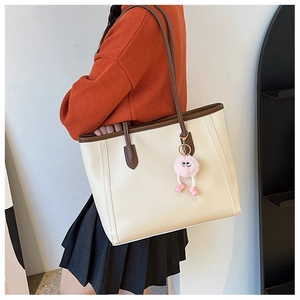 Detail of off-white tote bag with brown leather handles and pink plush keychain