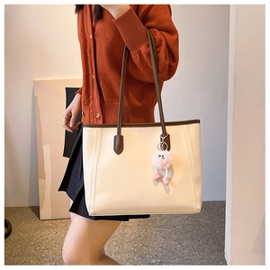 Close-up of cream tote bag with brown straps and pink plush pendant on a model