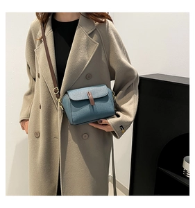 Detail of misty blue leather crossbody bag with lychee texture and brown buckle