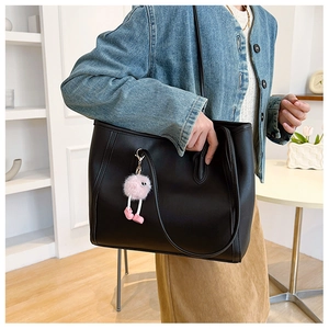 Matte black tote bag featuring a cute pink plush monster charm in a bright indoor setting