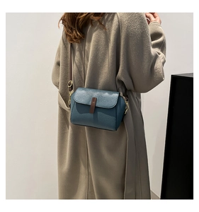 Gros plan d'un sac bandoulière bleu avec texture cuir litchi et boucle sur un manteau