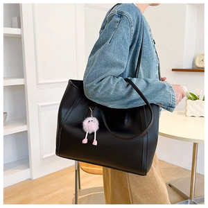 Minimalist black tote bag detail featuring a cute pink plush charm and side stitching