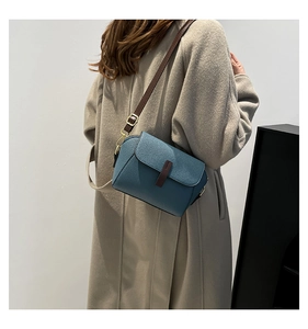 Détail de la texture cuir grainé bleu et de la bandoulière marron du sac à bandoulière