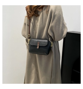 Detail of black pebbled leather small square bag with brown strap on female model