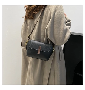 Detail of black pebbled leather crossbody bag with brown strap on a beige coat model