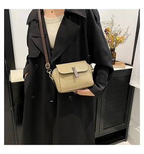 Détail du sac bandoulière beige en cuir grainé avec sangle marron sur un trench-coat noir