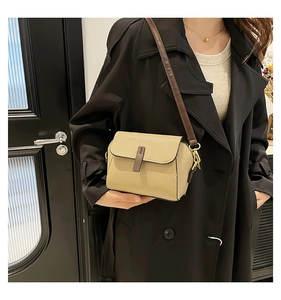 Petit sac carré en cuir à motif litchi porté par un mannequin sur un trench noir