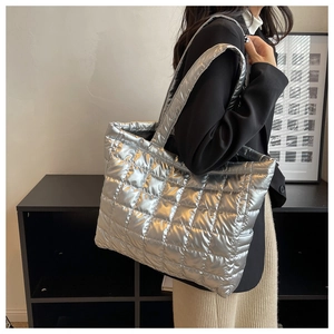 Close-up of a silver quilted puffer tote bag with wide shoulder strap in modern setting